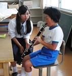 中学生が小学生に楽器の演奏の仕方を教えている写真